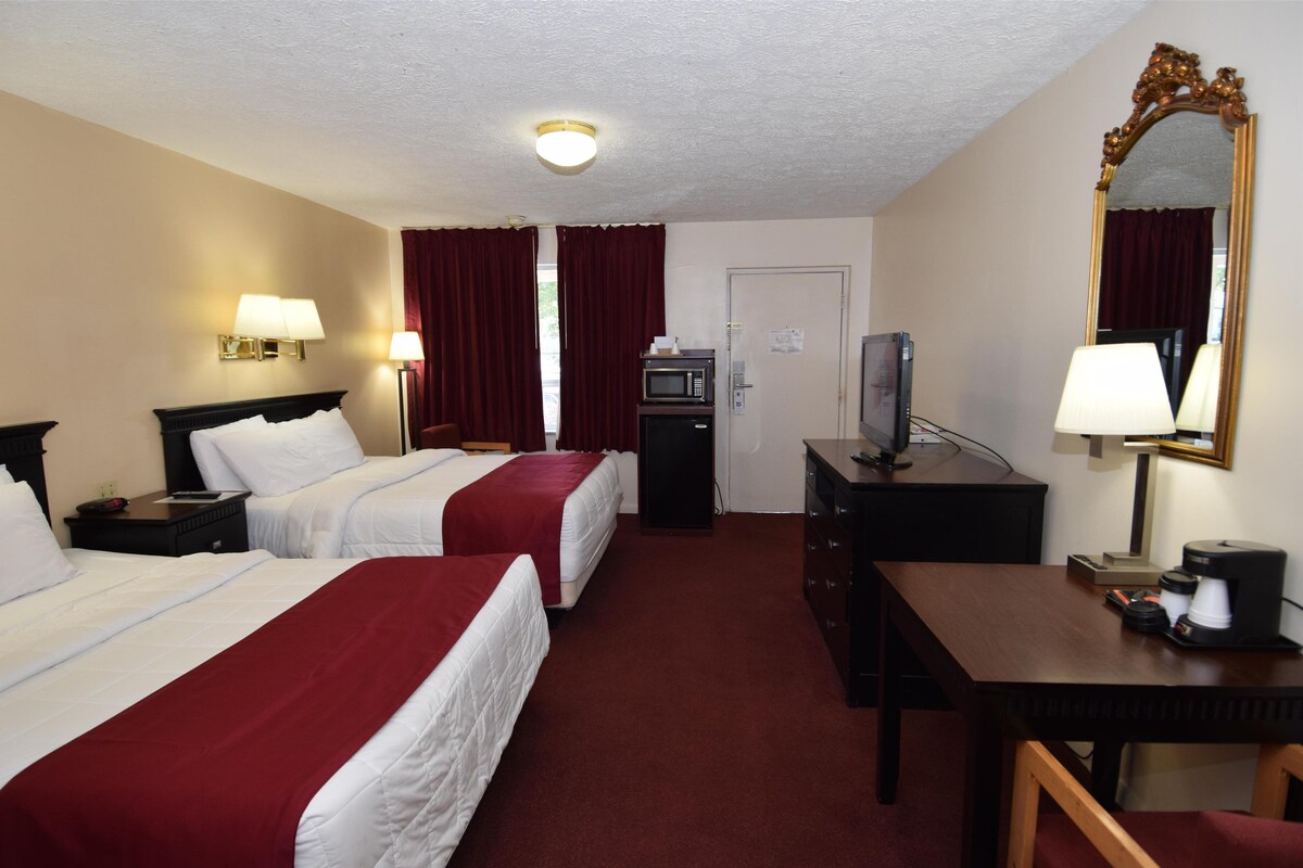A hotel room with two beds, a desk, a TV, a microwave, and a mirror.
