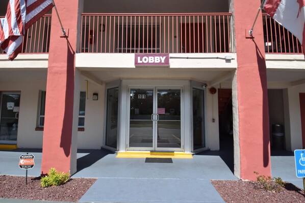 Entrada de un edificio con un cartel que dice 'Lobby', una rampa accesible para sillas de ruedas y un cartel de 'Estacionamiento'.