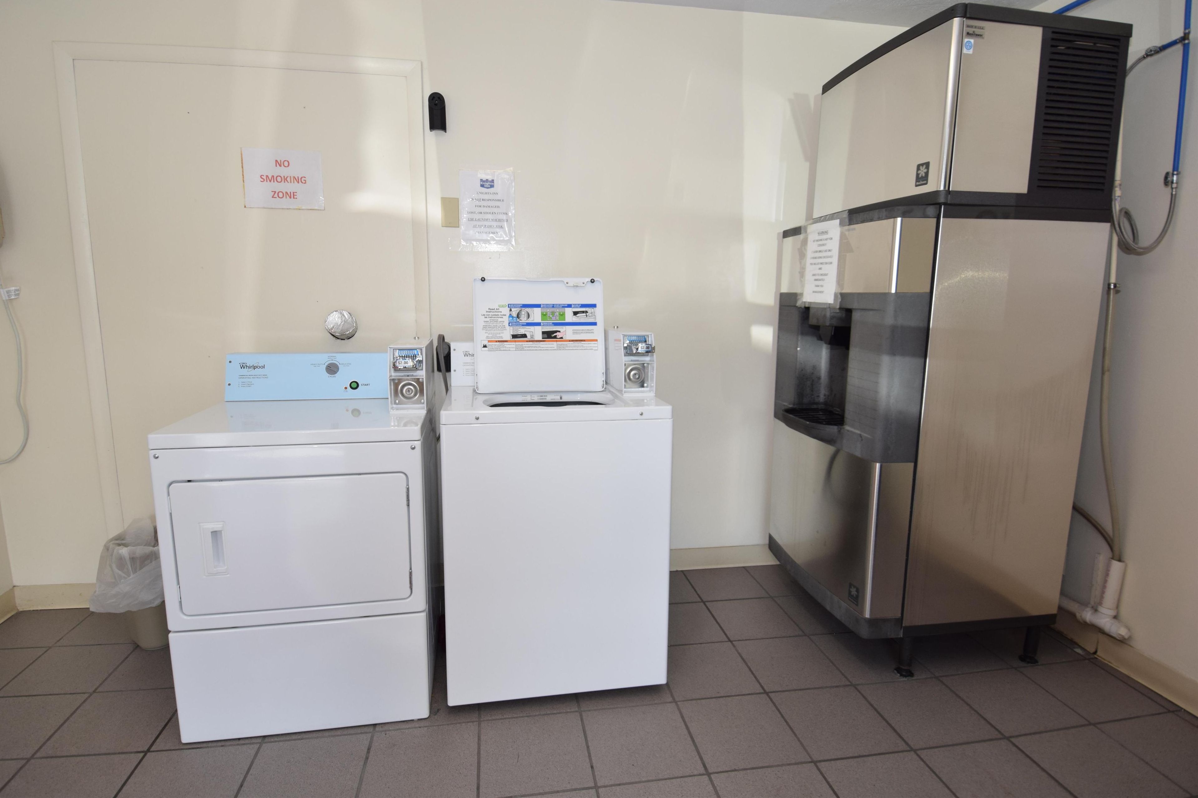 A laundry area with a Whirlpool washer and dryer, a stainless steel refrigerator, and a "No Smoking" sign on the wall.