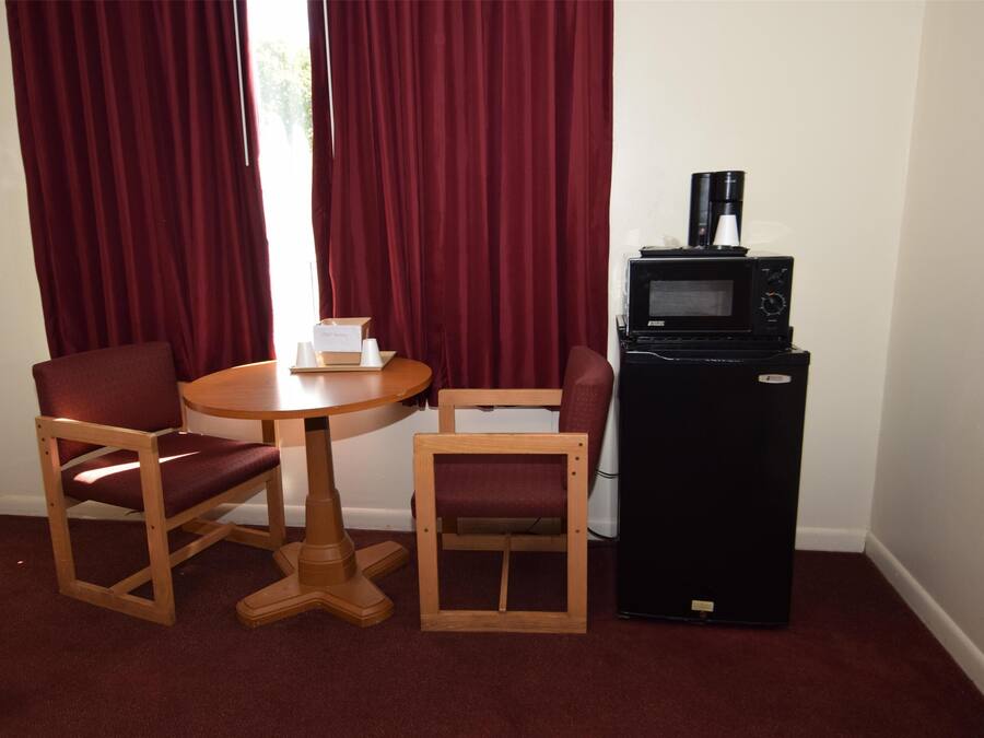 Une pièce avec une table en bois et deux chaises, un réfrigérateur noir et une fenêtre avec des rideaux rouges.