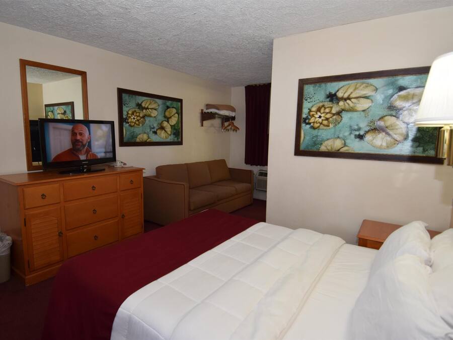 A hotel room with a bed, a TV, a dresser, a chair, and two paintings on the walls.