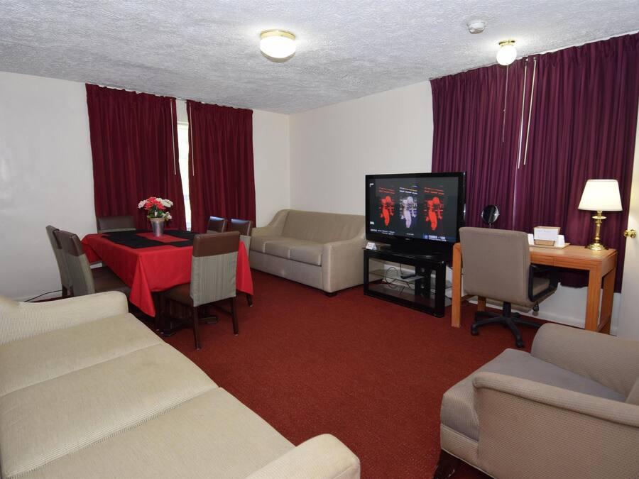 A hotel room with a living area featuring a sofa, a dining table with chairs, a television, and a desk with a lamp.