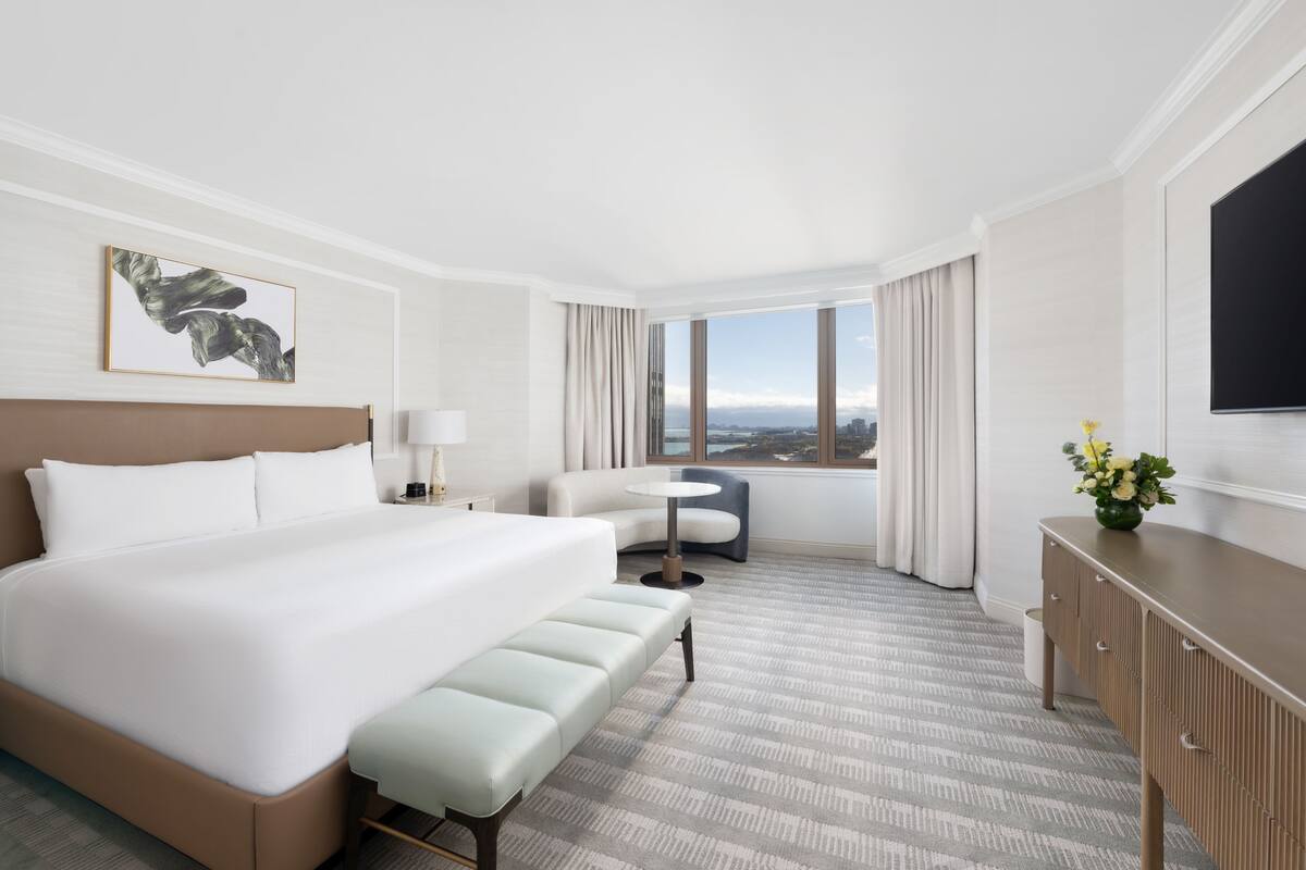 Habitación de hotel con una cama grande, un escritorio, una silla, una mesita y vistas a la ciudad.