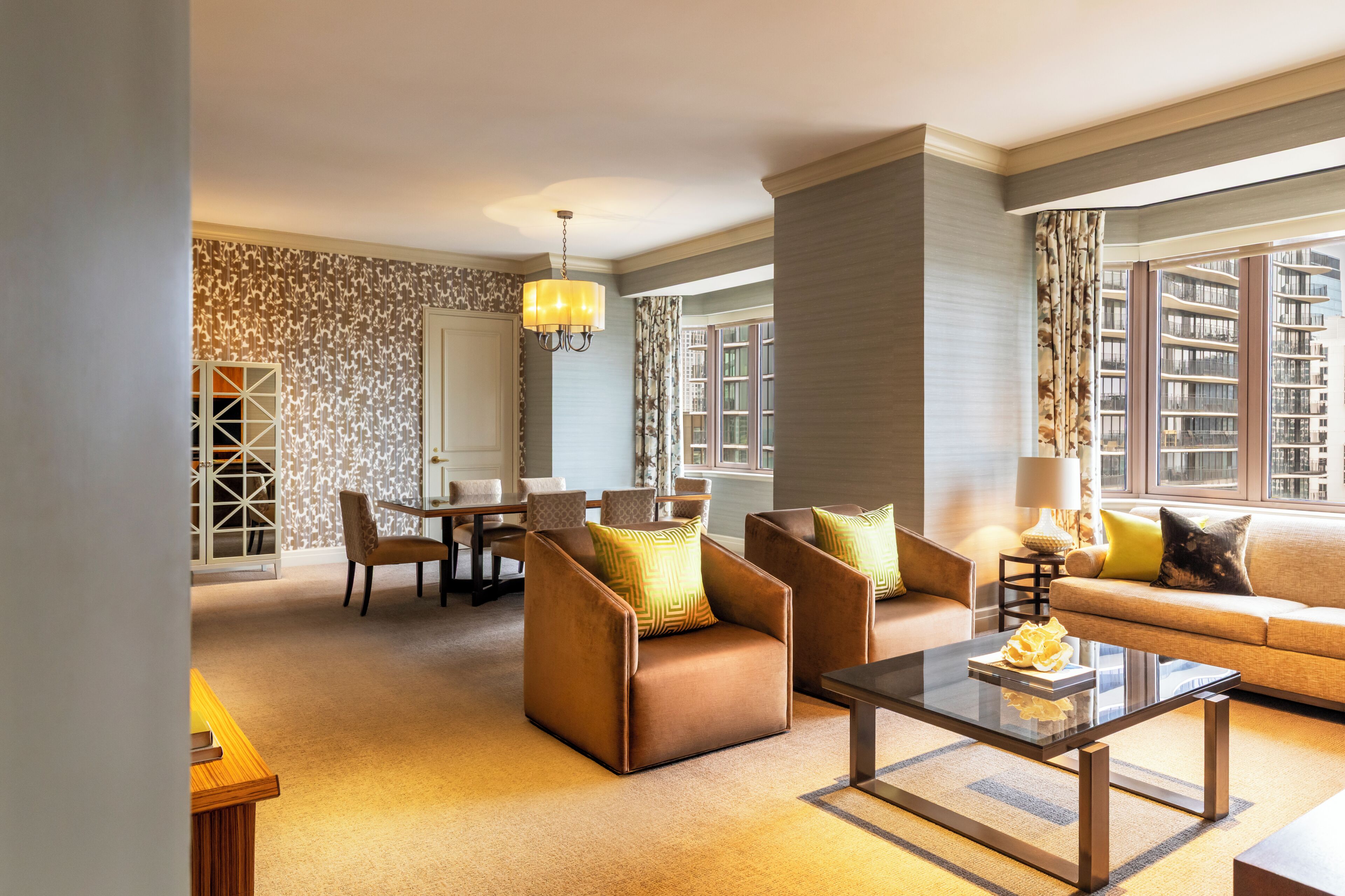 Una habitación de hotel moderna con sofá, sillones, una mesa de comedor y una araña.