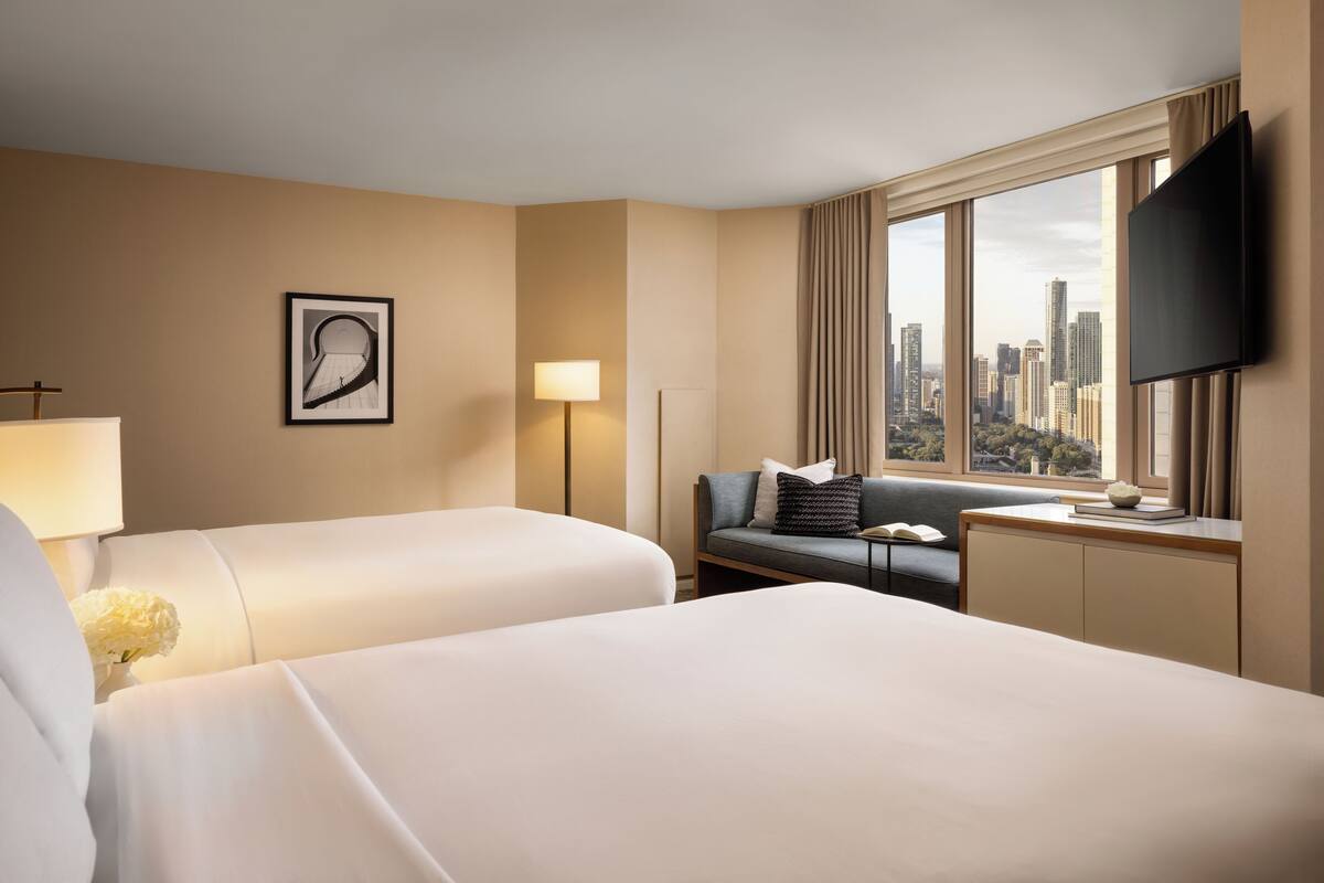 Habitación de hotel con dos camas, un sofá, televisión y vistas a la ciudad.