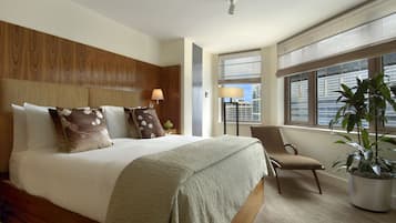 Habitación de hotel con una cama grande, una silla, una planta en maceta y una ventana con vistas a la ciudad.