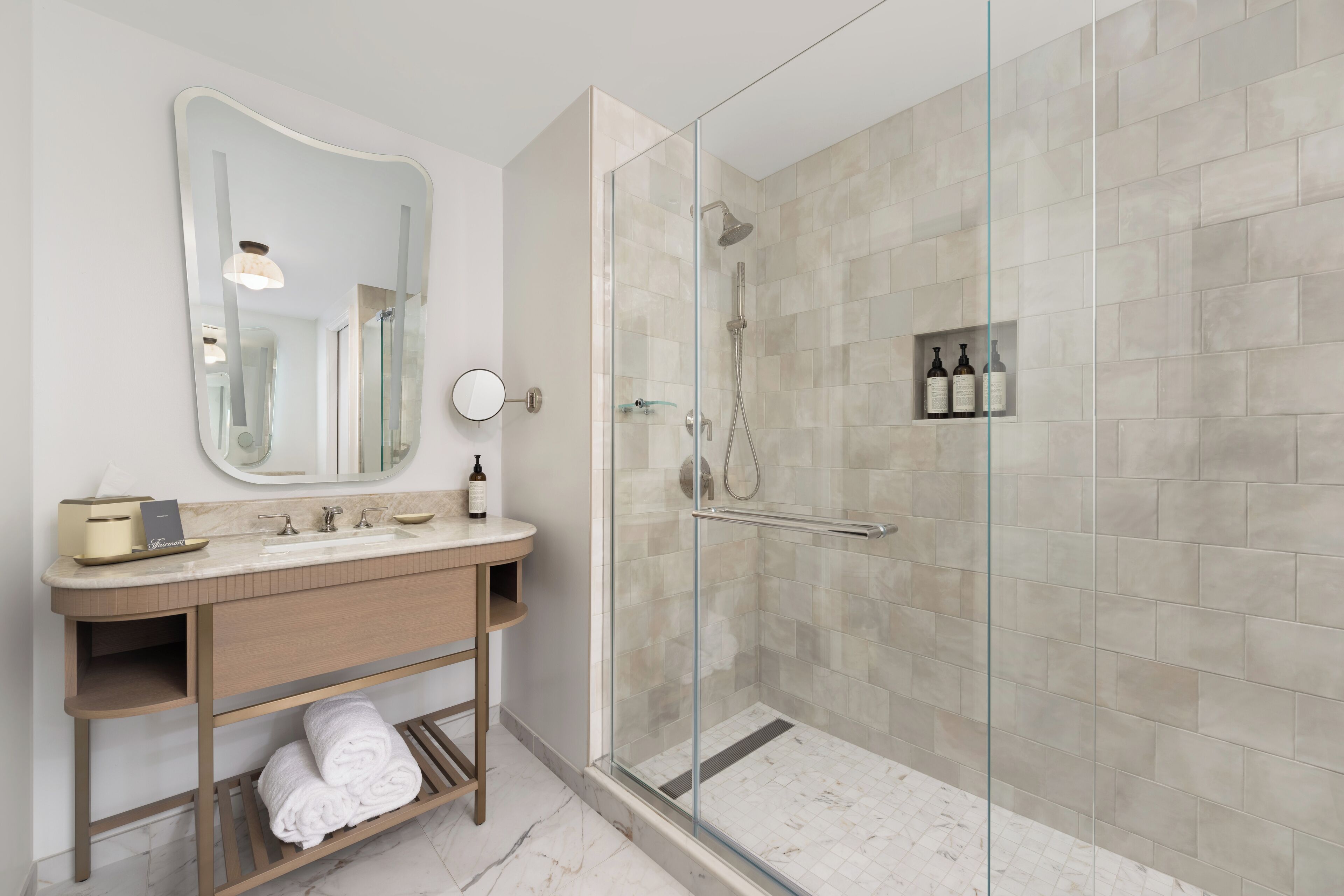 Een moderne badkamer met een douche in een glazen cabine, een wastafel met spiegel en een plank met toiletartikelen.