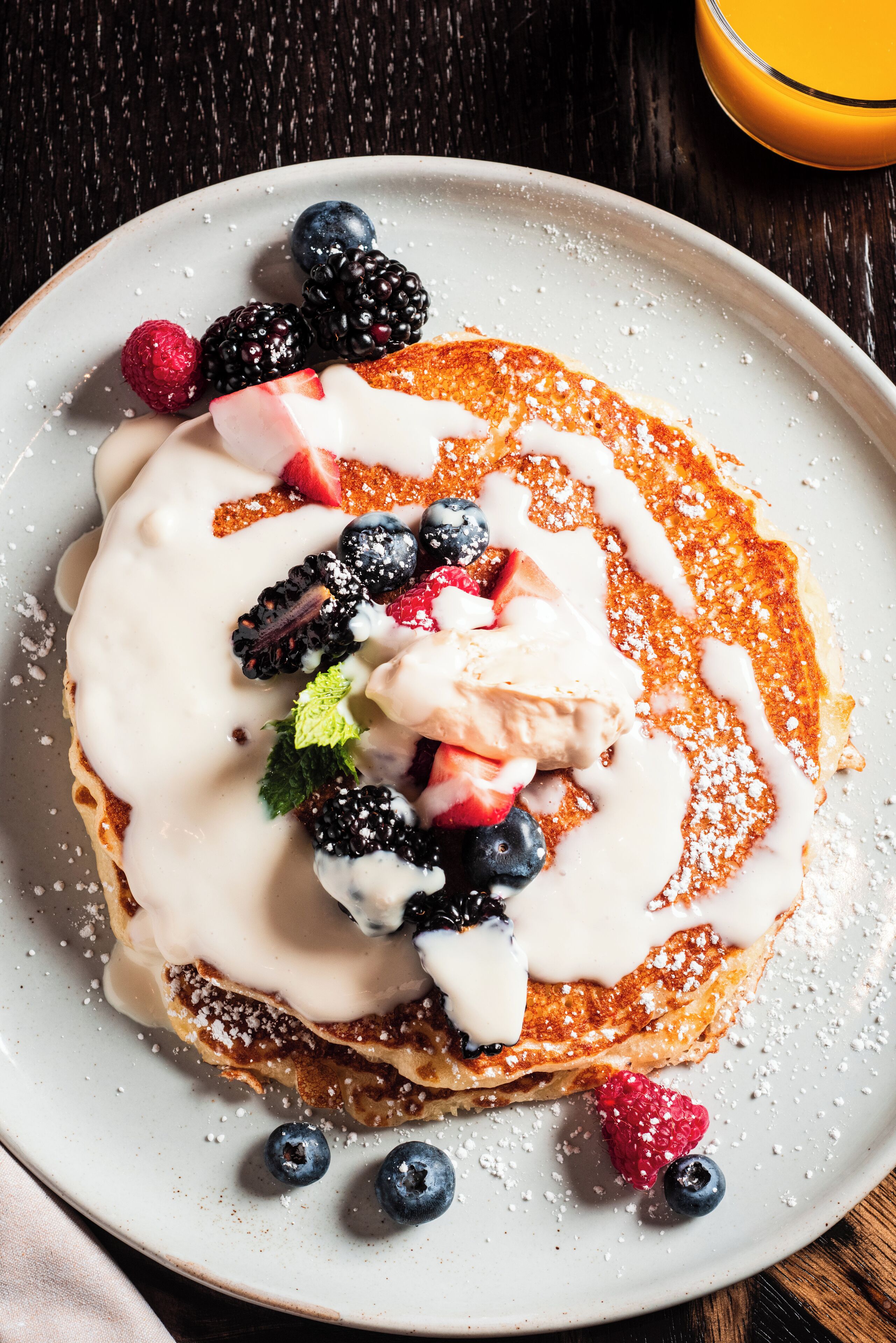 A plate of pancakes topped with berries, whipped cream, and a dusting of powdered sugar.