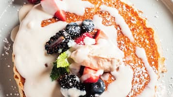 A plate of pancakes topped with berries, whipped cream, and a dusting of powdered sugar.