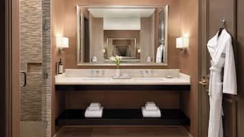 Un baño moderno con un espejo grande, dos lavamanos, una ducha y una bata colgada en la puerta.