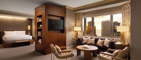 A hotel room with a bed, a TV, a sofa, two armchairs, a coffee table, and a city view.