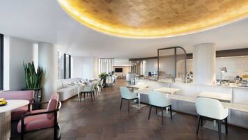 A modern hotel lobby with a central seating area, a bar, and a kitchen visible in the background.