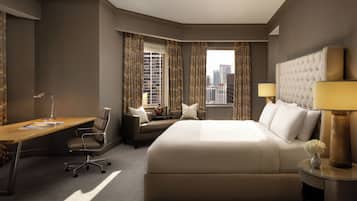A hotel room with a large bed, a desk, a chair, a sofa, and a view of the cityscape.