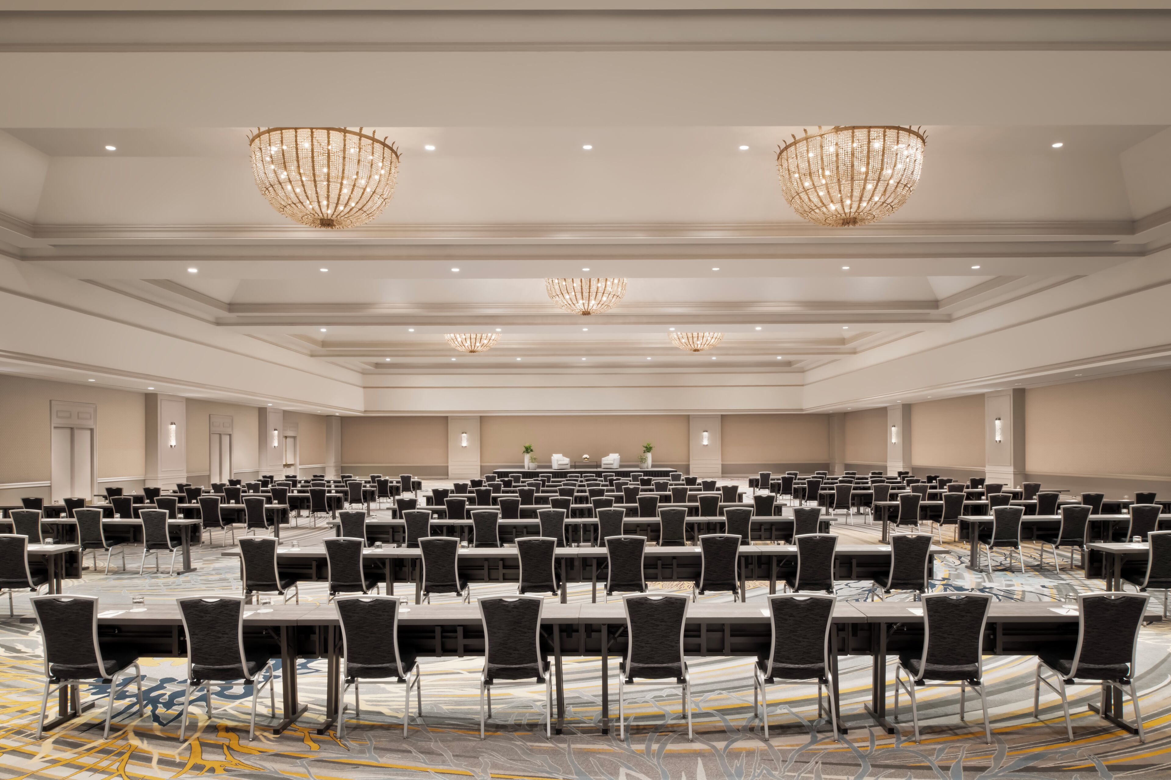 Une grande salle de conférence avec de longues rangées de tables et de chaises, des lustres et un éclairage encastré.