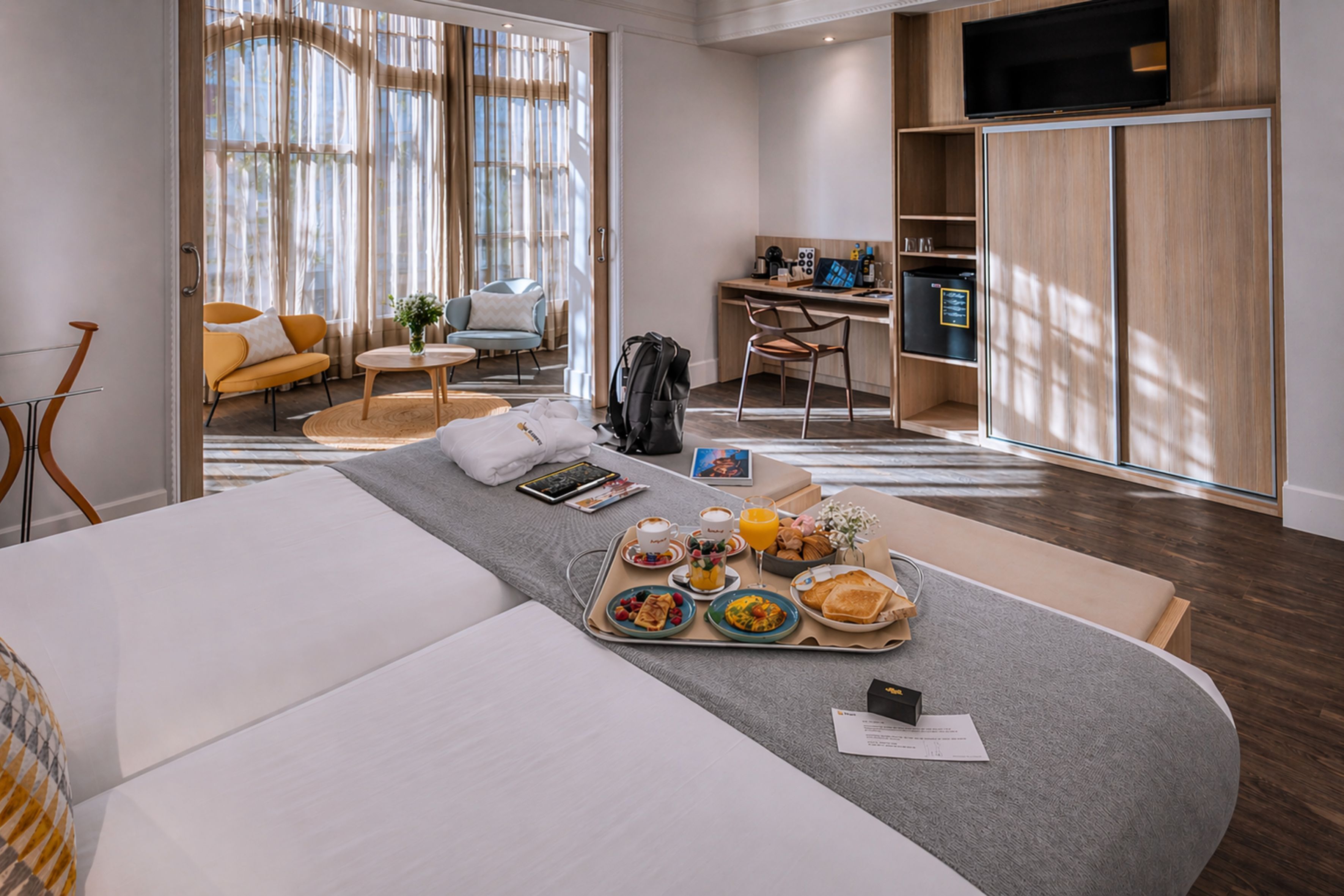 A hotel room with a bed, breakfast tray, desk, and a TV.