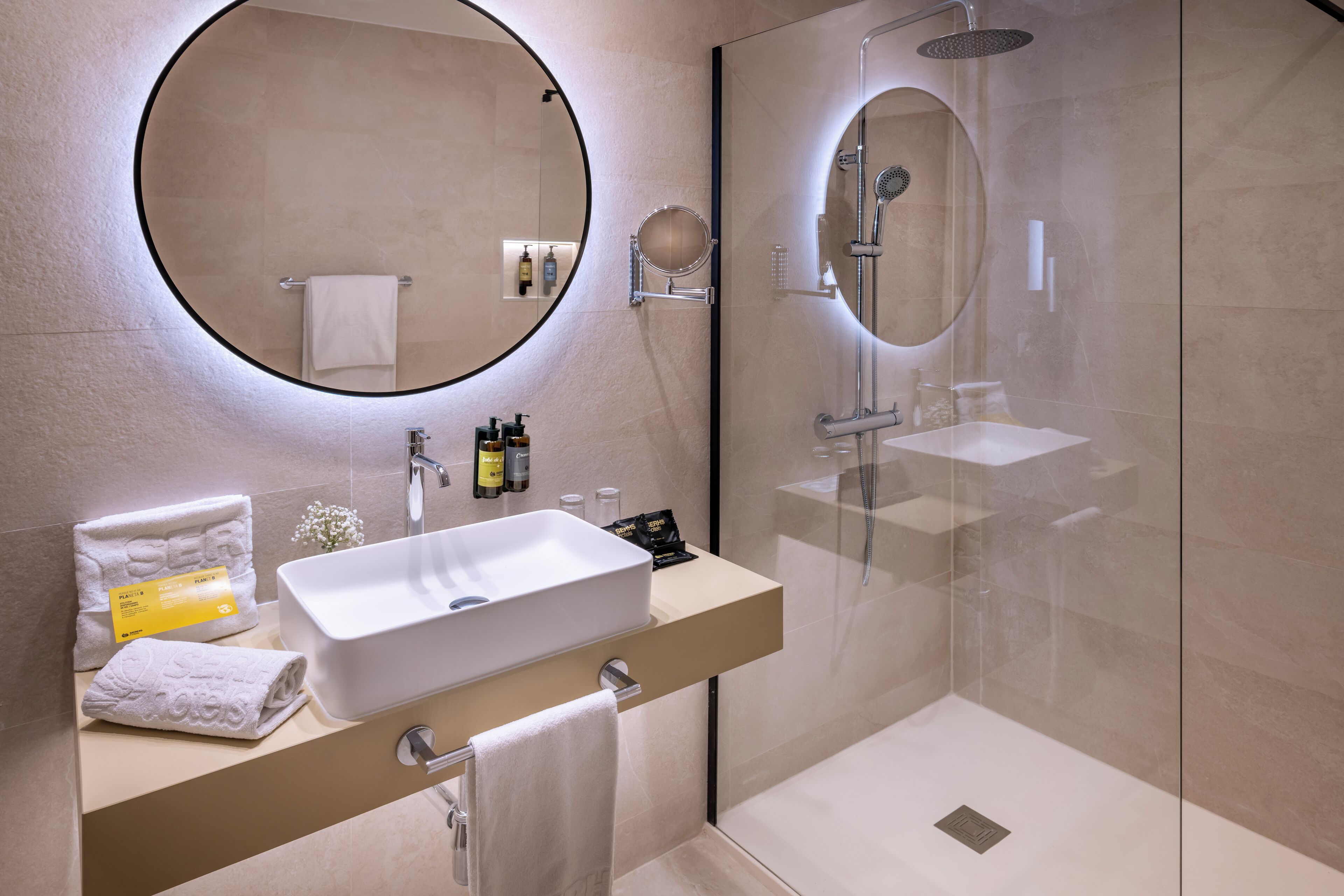 Un baño moderno con un espejo grande, un lavamanos y una ducha con mampara de vidrio.