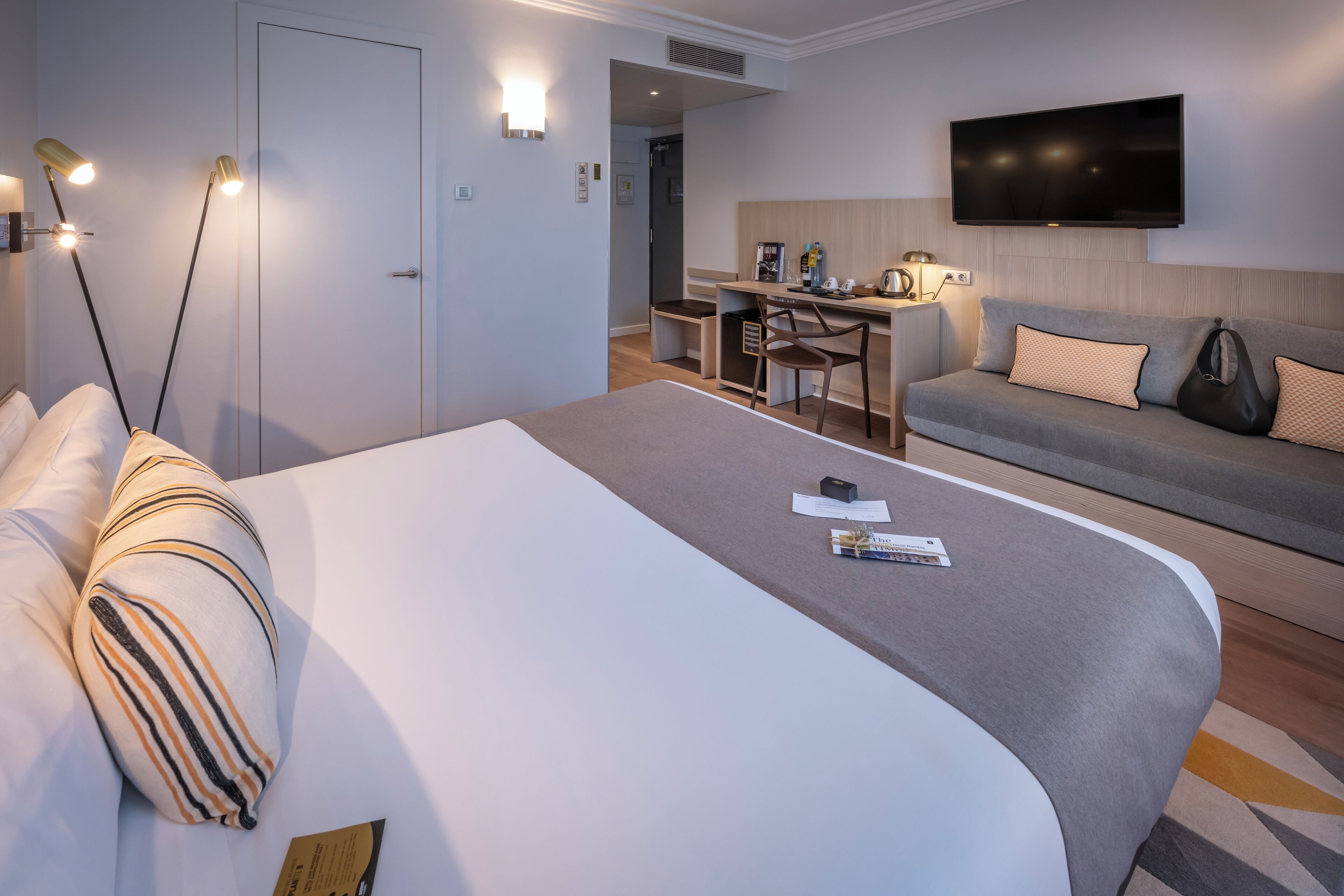 Quarto de hotel com cama grande, escrivaninha, sofá e televisão.