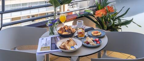 A balcony table with breakfast items, a newspaper, and a view of the cityscape.