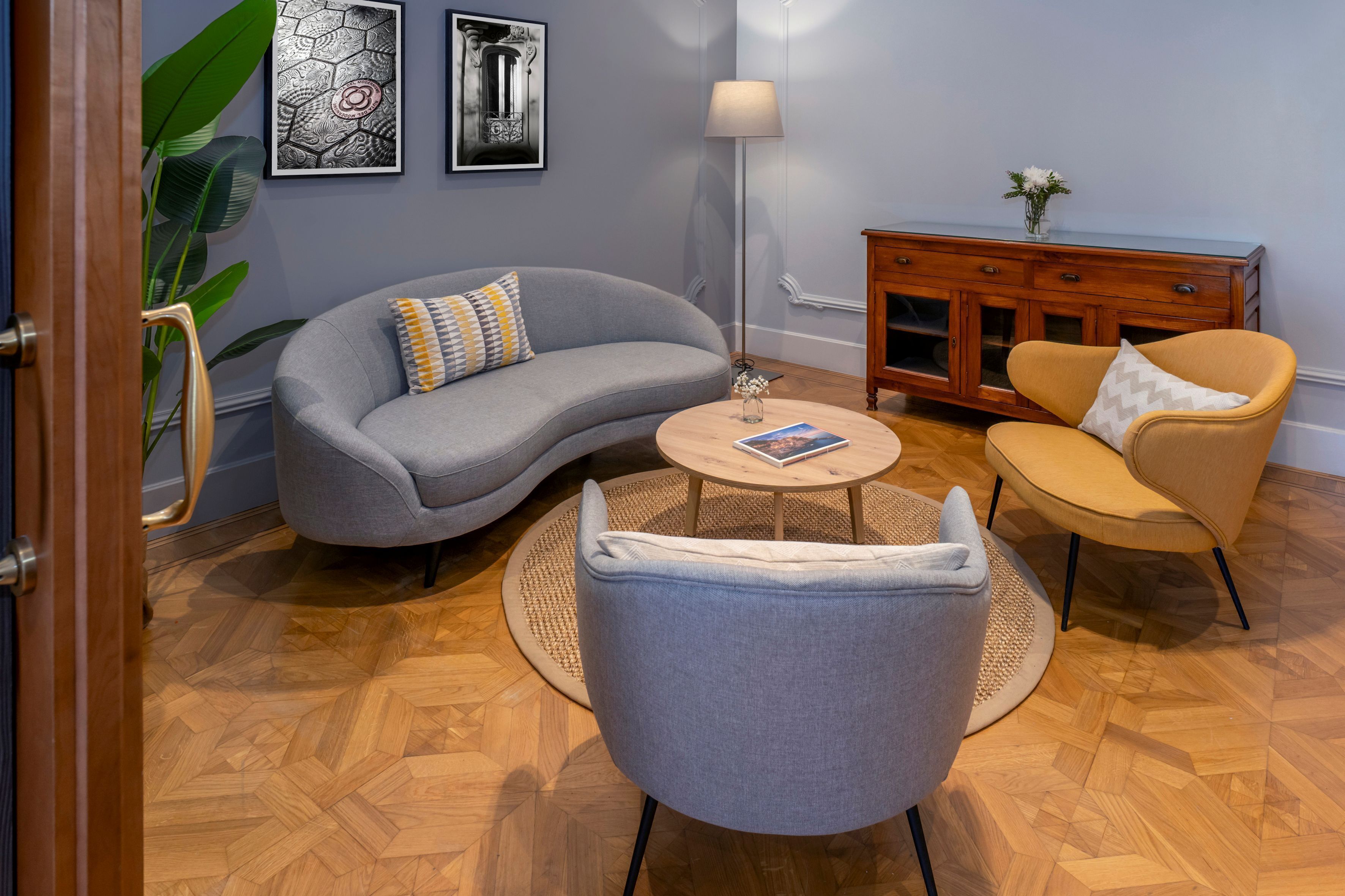 A living room with a grey sofa, a round coffee table, a grey armchair, a wooden cabinet, and a floor lamp.