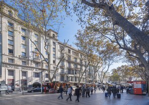 A hotel with a classical facade, multiple floors, and a pedestrian area with trees and shops. - Hotel SERHS Rivoli Rambla (Barcelona)