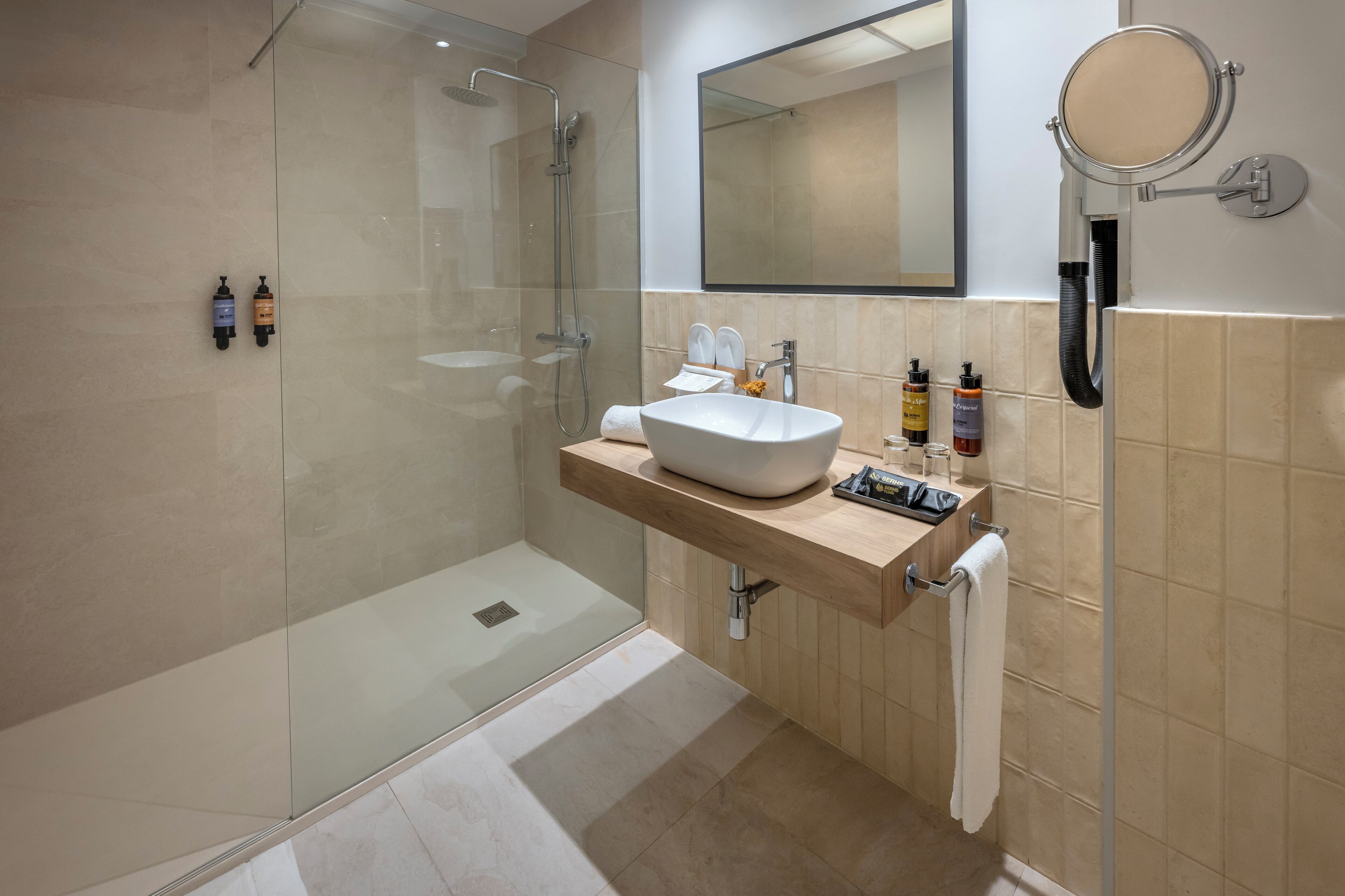 A modern bathroom with a glass-enclosed shower, a large mirror, and a beige tiled wall.