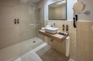Un baño moderno con ducha de vidrio, un espejo grande y pared revestida de baldosas color beige.