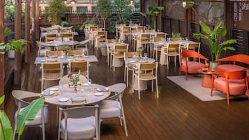 Een terras met meerdere tafels en stoelen, omgeven door houten vloerdelen en potplanten.