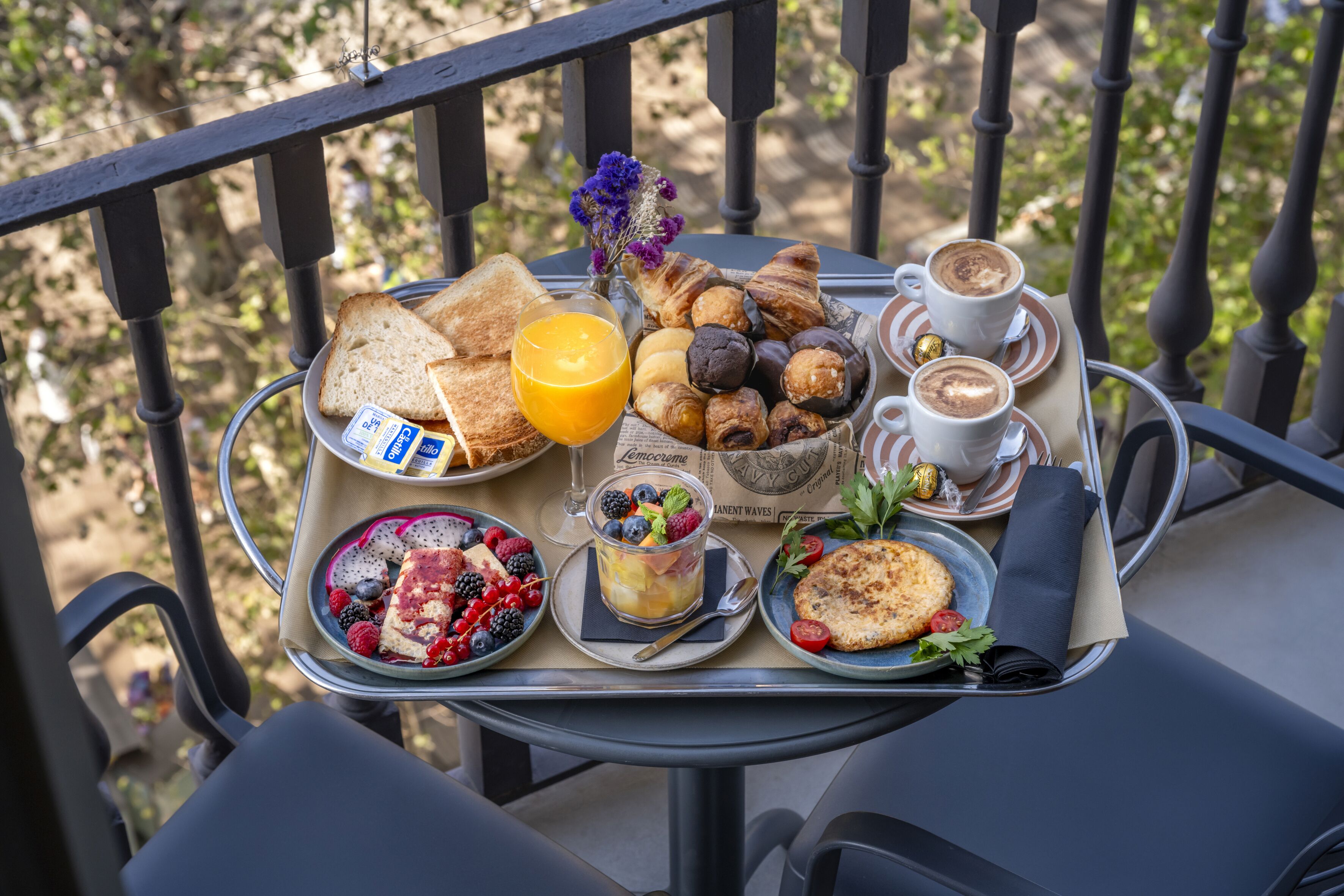 A tray with breakfast items including toast, croissants, muffins, and coffee on a balcony.