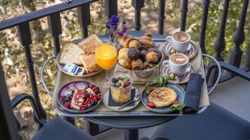 A tray with breakfast items including toast, croissants, muffins, and coffee on a balcony.
