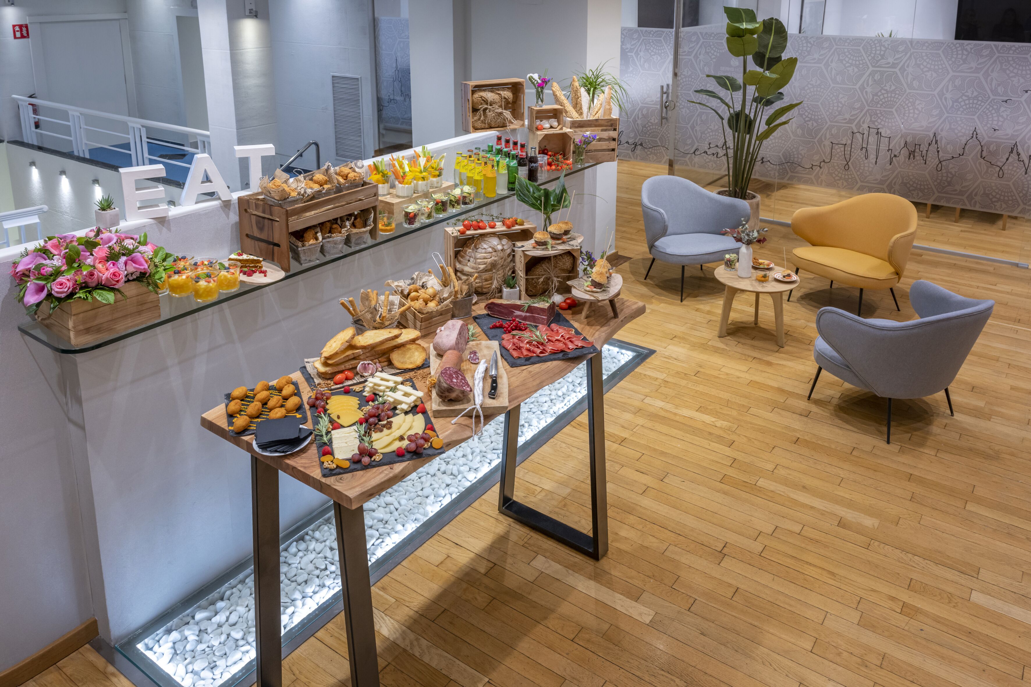 A buffet table with various food items and a seating area with two chairs and a small table.