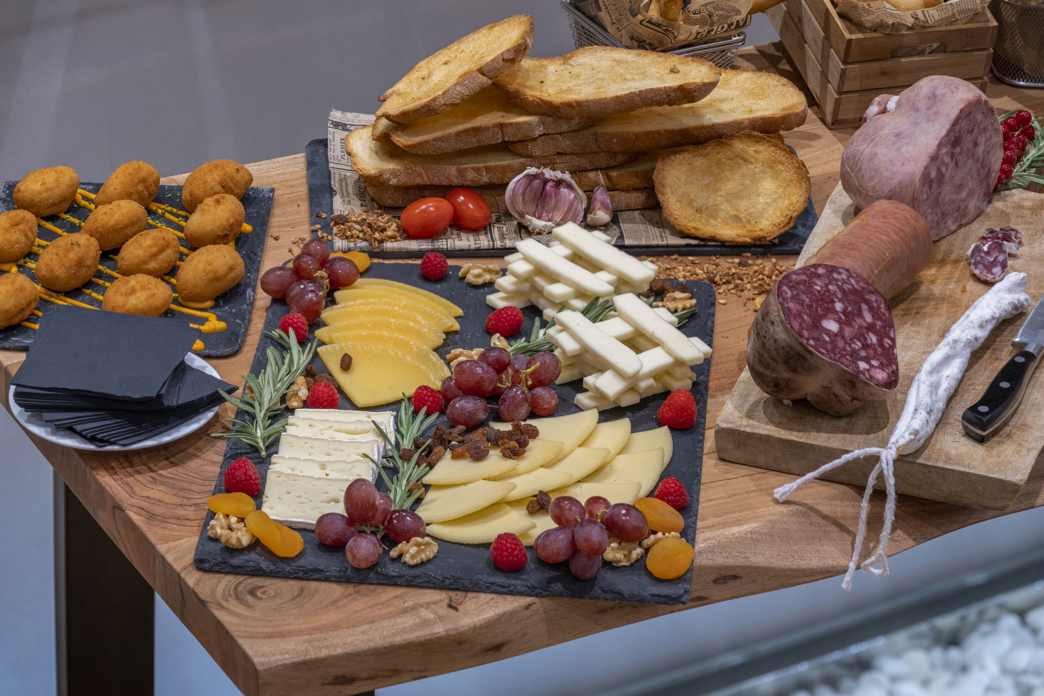 Una tabla de fiambres con quesos variados, frutas, frutos secos y embutidos.