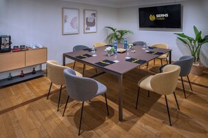 Sala de conferências com uma mesa comprida, seis cadeiras, máquina de café e uma televisão exibindo o logotipo do hotel.