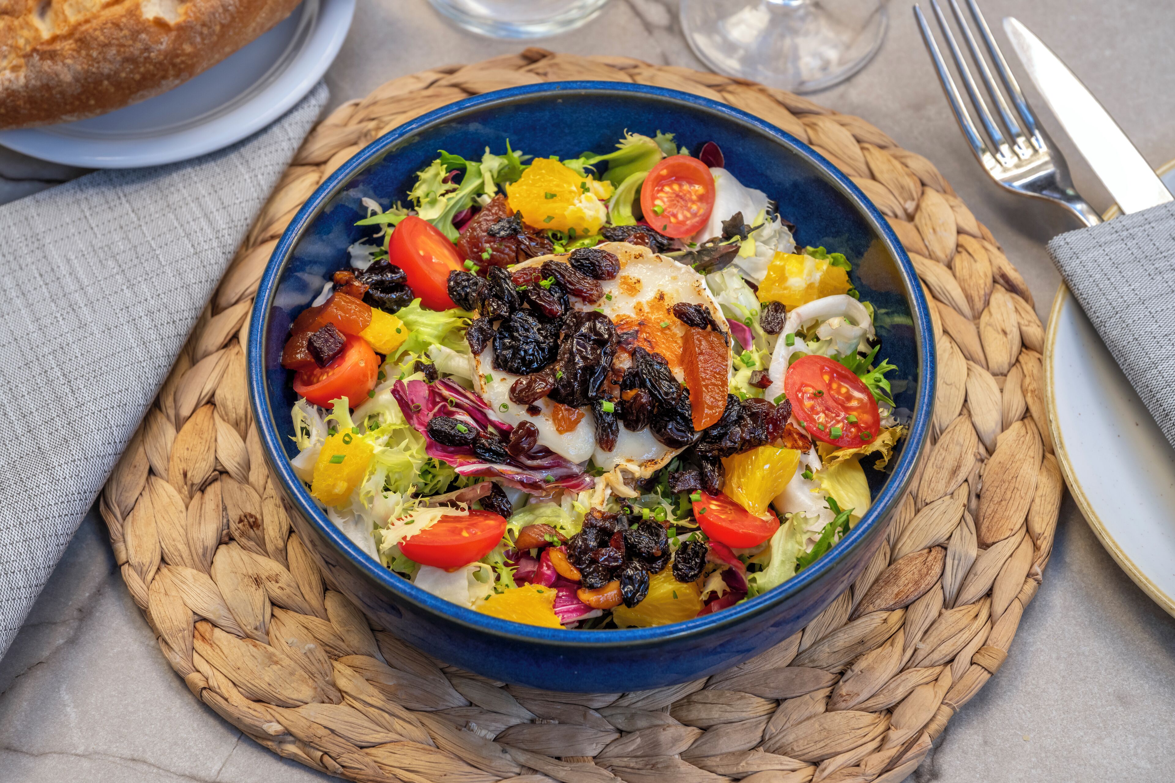 Un tazón de ensalada con diversas verduras y frutas sobre un camino de mesa tejido.
