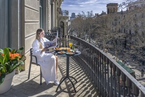 Un balcón con una mesa dispuesta para el desayuno, una planta en maceta y vistas de la ciudad.