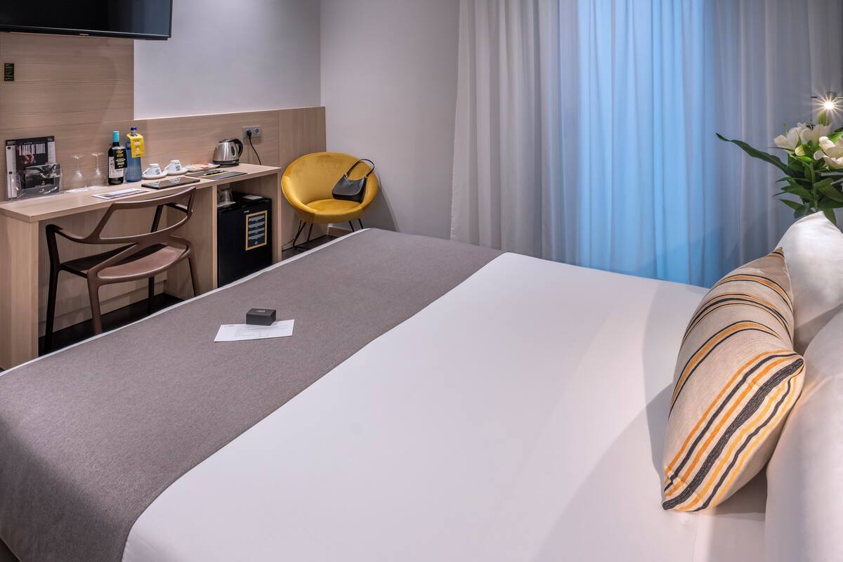 A hotel room with a bed, a desk, a chair, and a TV.