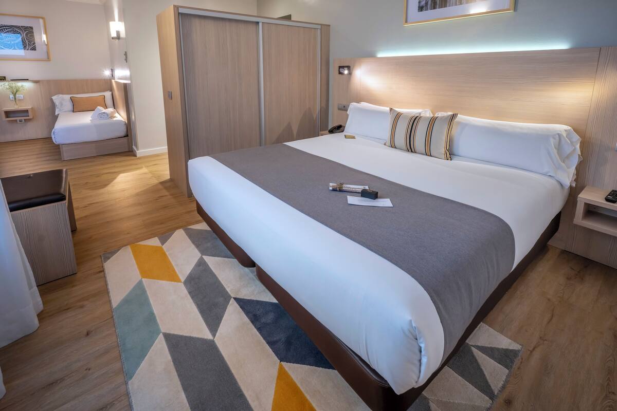 A hotel room with a large bed, a bedside table, a nightstand, a wardrobe, and a small seating area.