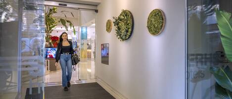 Un hall d’hôtel moderne avec une entrée en verre, un comptoir d’accueil et des œuvres d’art décoratives sur les murs.