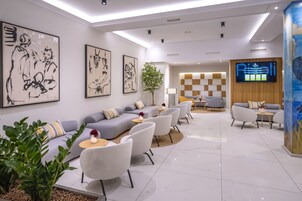 A modern hotel lobby with a grey sofa, white armchairs, a coffee table, and artwork on the walls.