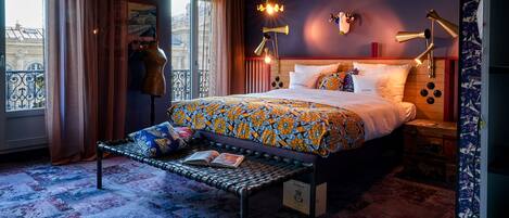 A modern hotel room with a large bed, a bench, and a view of the city.