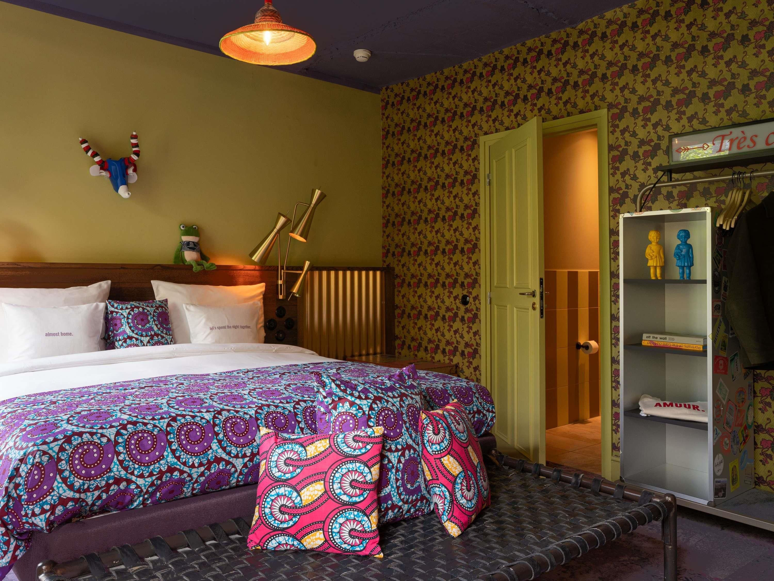 Una cama con ropa de cama estampada, una lámpara de noche y una repisa con figuritas.