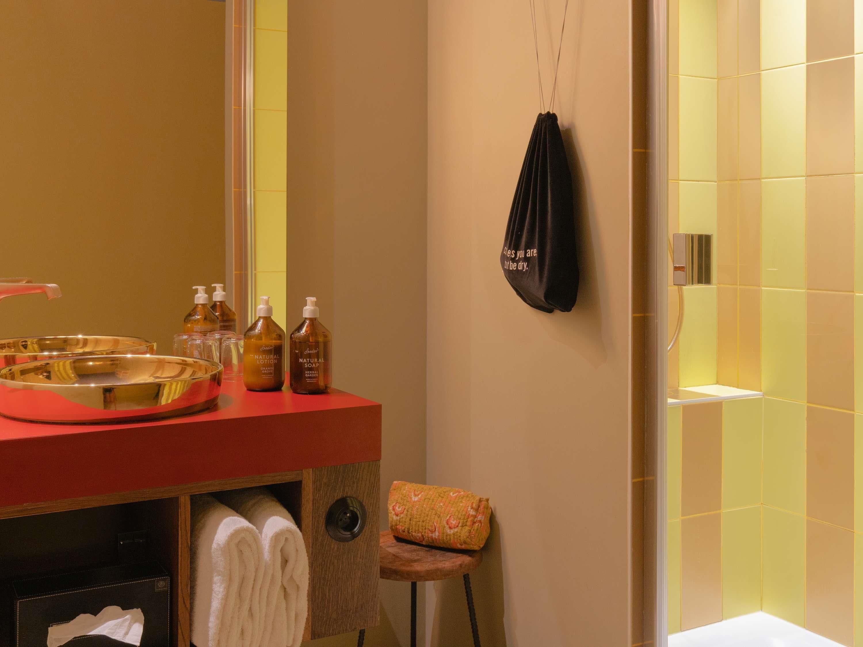 Un baño con lavamanos rojo, artículos de aseo, un perchero y zona de ducha.