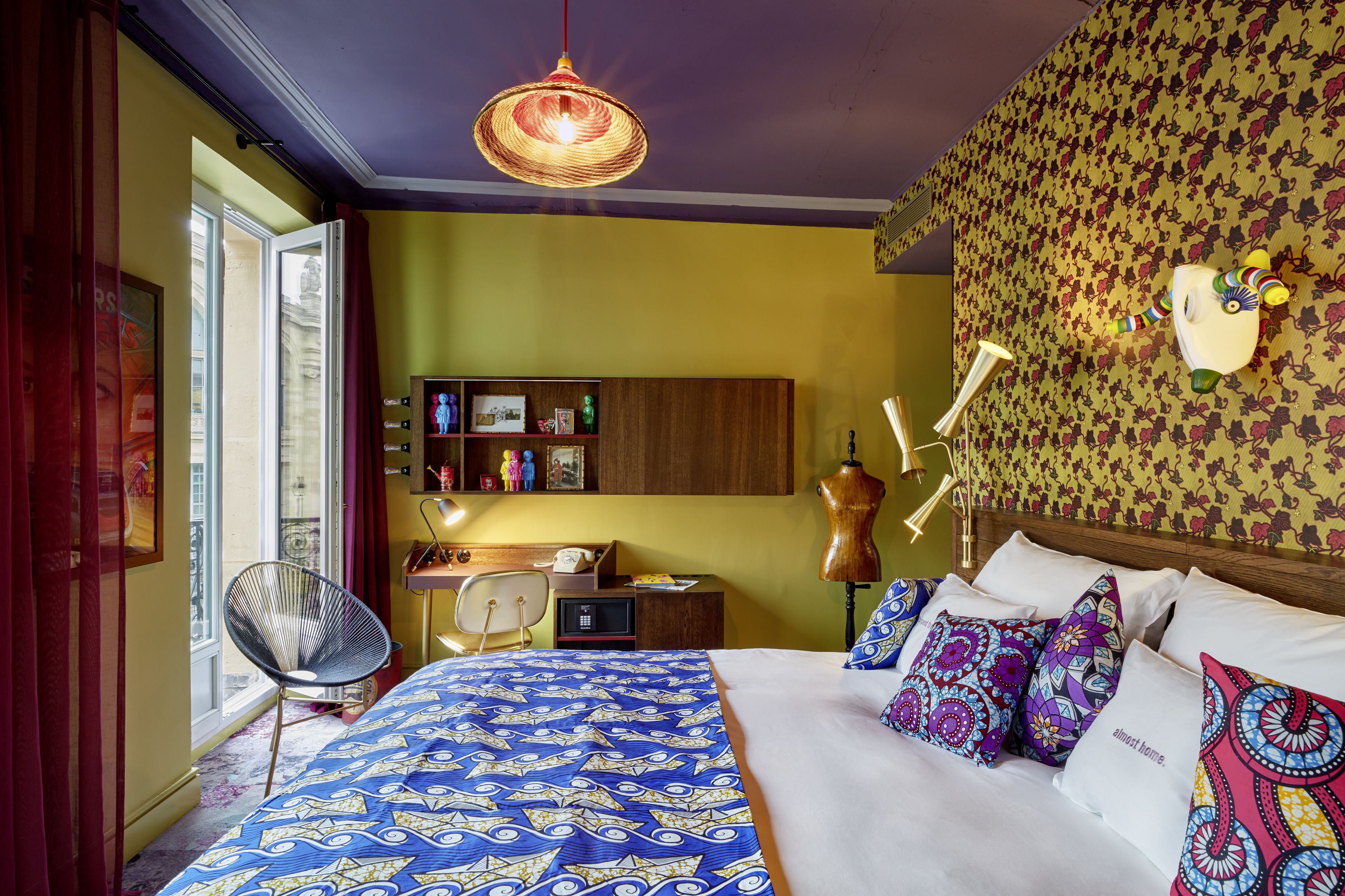 A room with a bed, a desk, a chair, and a wall with a decorative headboard.
