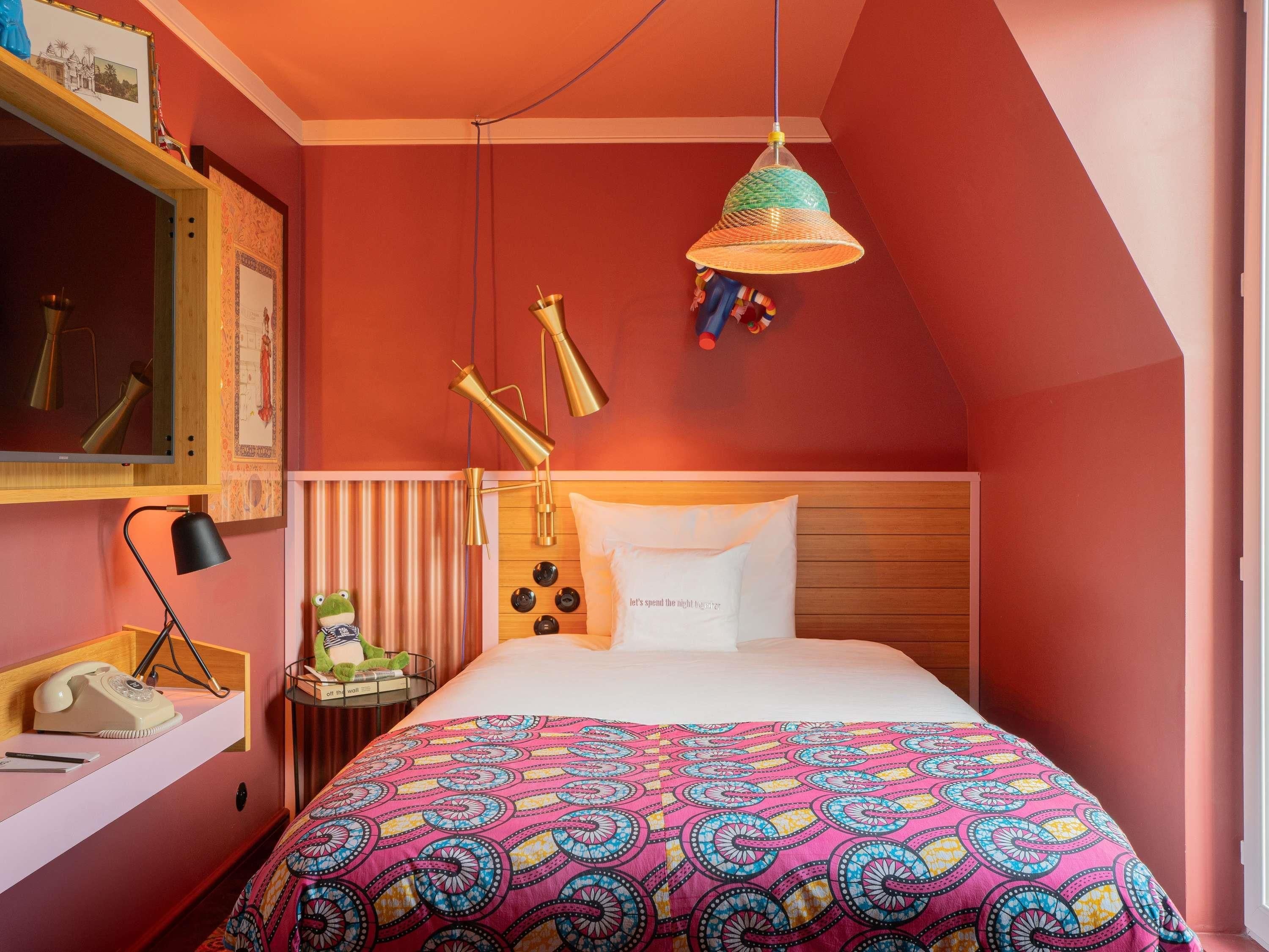 A bedroom with a bed, a nightstand, a lamp, a hanging light, and a wall-mounted shelf.