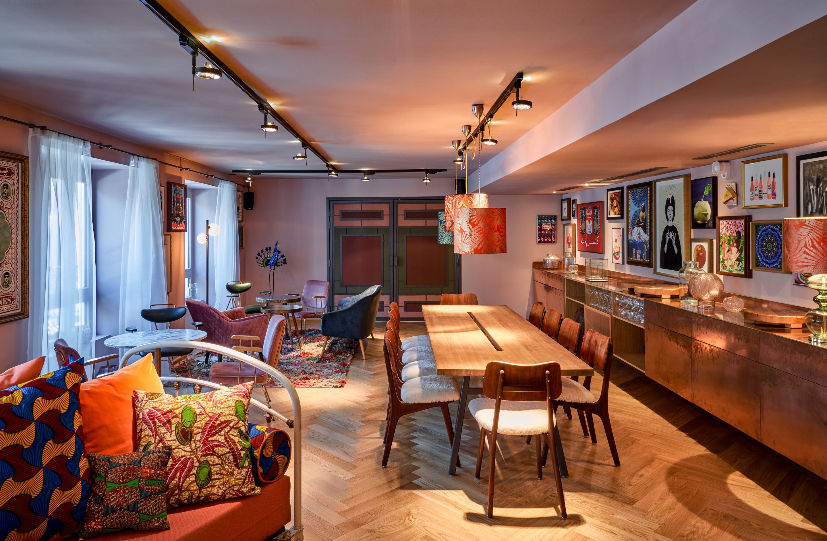 Un espace de restauration moderne avec une table et des chaises en bois, un comptoir de bar et diverses œuvres d’art accrochées aux murs.