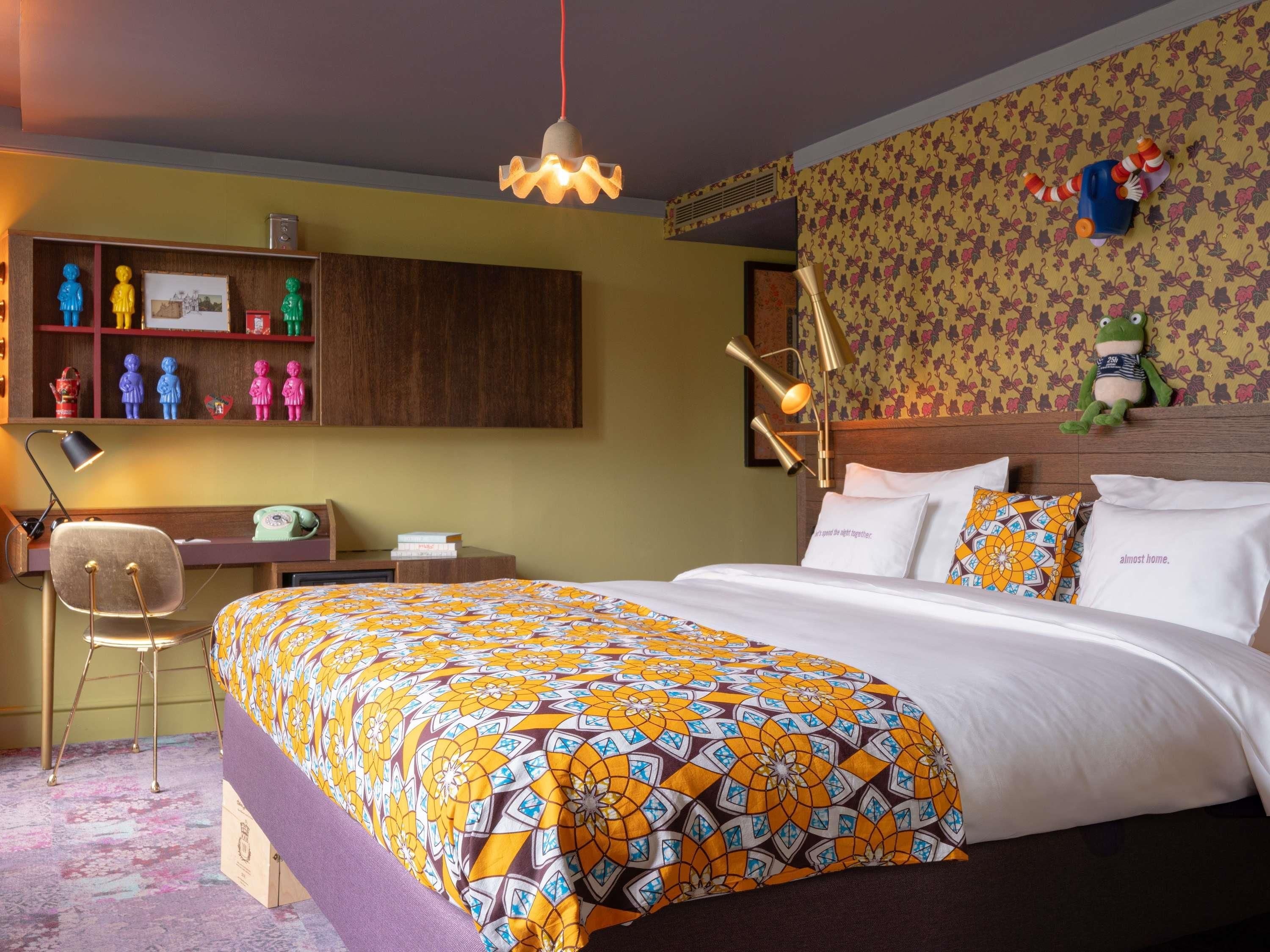Una habitación de hotel con cama, escritorio, silla y una pared decorada con figuritas de colores.