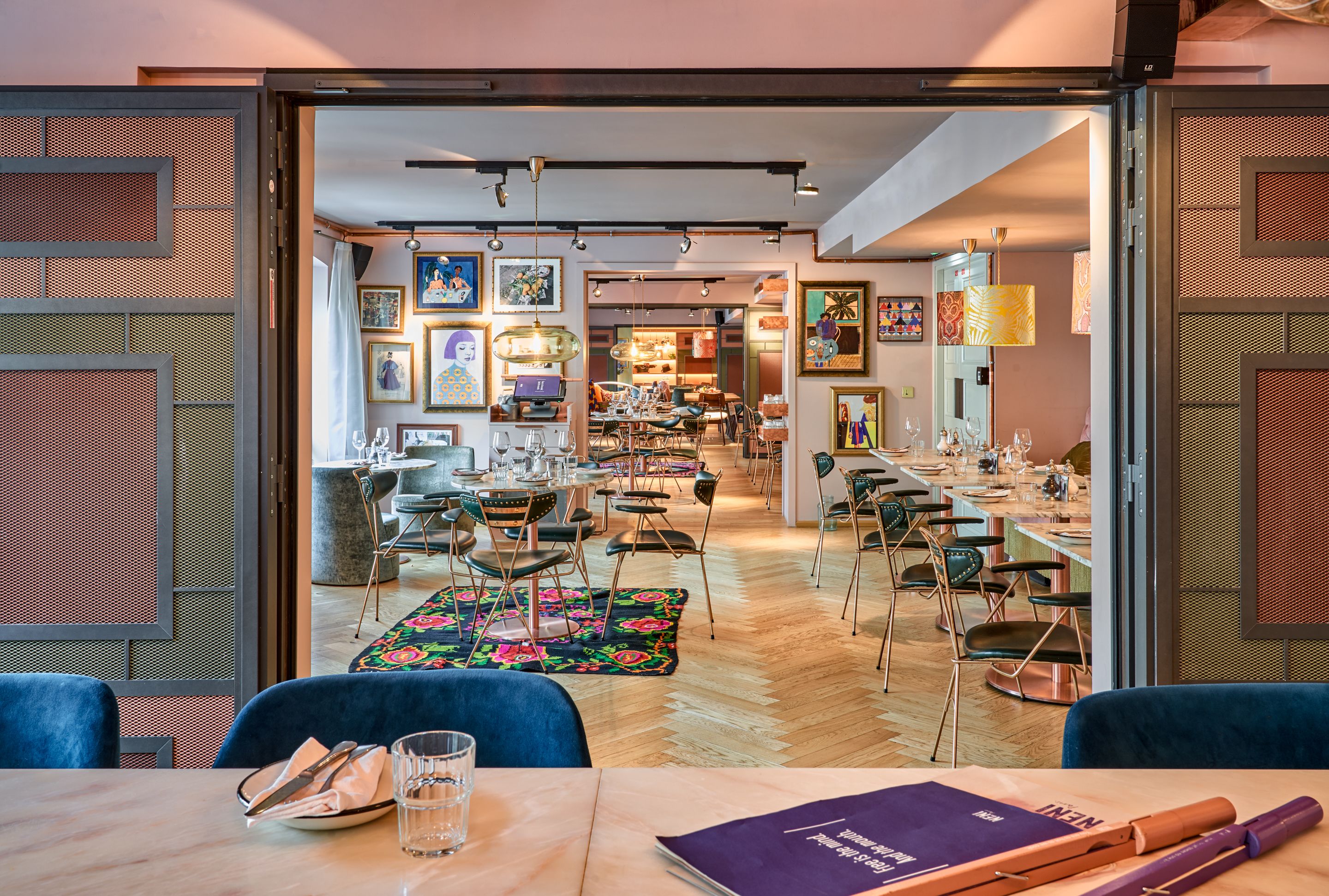 A spacious dining area with multiple tables and chairs, a colorful rug, and various artworks on the walls.