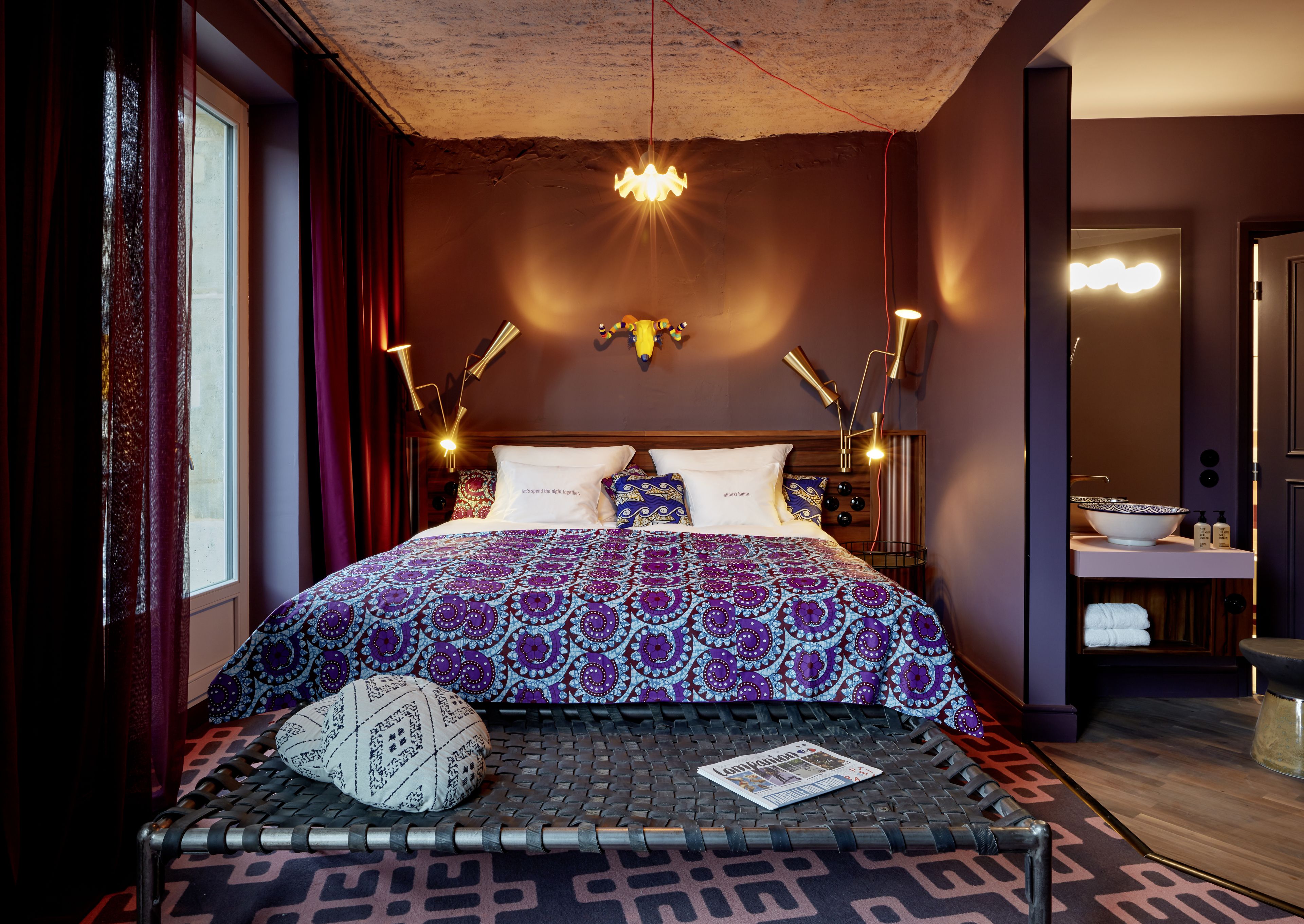 Una habitación de hotel moderna con una cama grande, ropa de cama con diseño, un diseño de techo único y un área de baño visible.