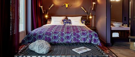 Una habitación de hotel moderna con una cama grande, ropa de cama con diseño, un diseño de techo único y un área de baño visible.