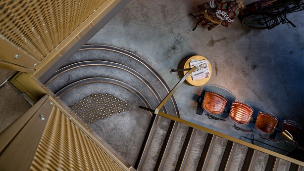 Eine Treppe führt zu einer Sitzecke mit Tisch und Stühlen, einem Fahrrad und einem gemusterten Teppich.