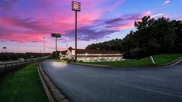 A Red Roof Inn with a large sign, located beside a highway with a grassy area and trees.